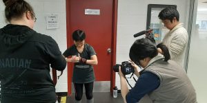 Student filmmakers surround subject Monica Ma in front of a red door at YMCA