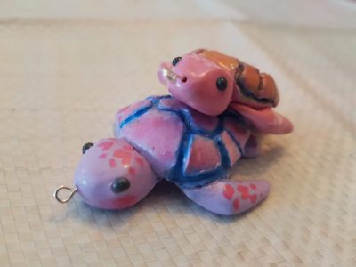 Polymer clay turtles stacked on top of each other. The turtle with the colours of the bisexual pride flag sits under the turtle with the colours of the pansexual pride flag.