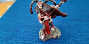 A lich figurine holding a bloody mace leans forward, a cape flowing behind it.